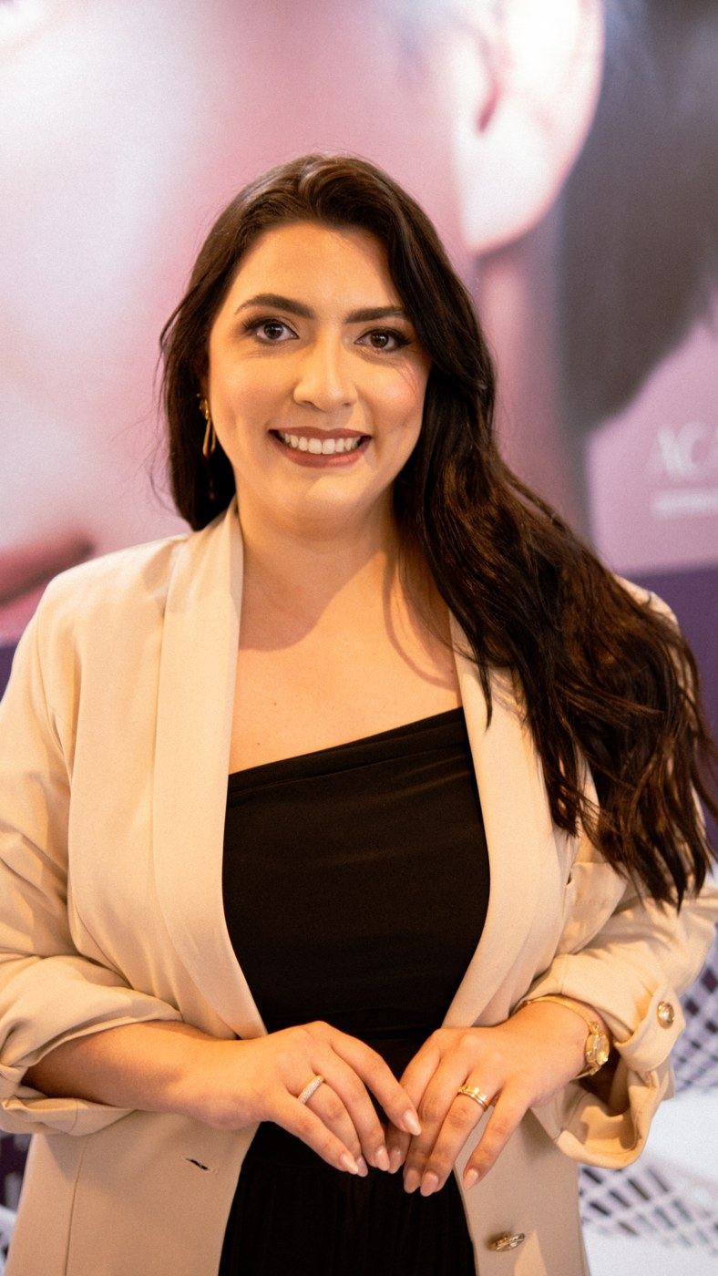 Alana Karine sorrindo, de blazer bege e vestido preto
